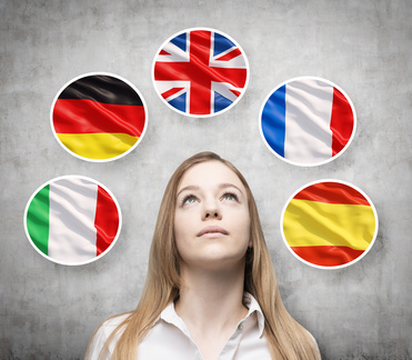Beautiful lady is surrounded by bubbles with european countries’ flags (Italian, German, Great Britain, French, Spanish). Learning of foreign languages concept. Concrete background.